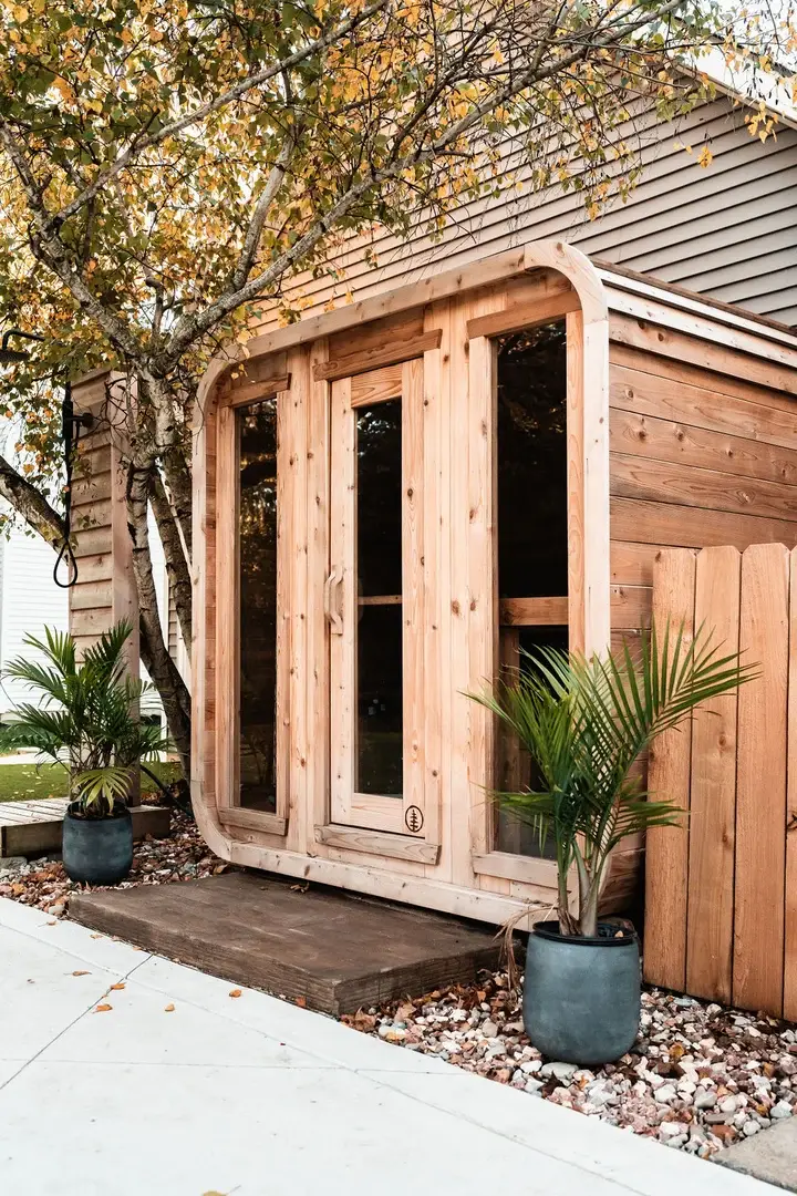 A cedar sauna cabin outside a house, framed by planters