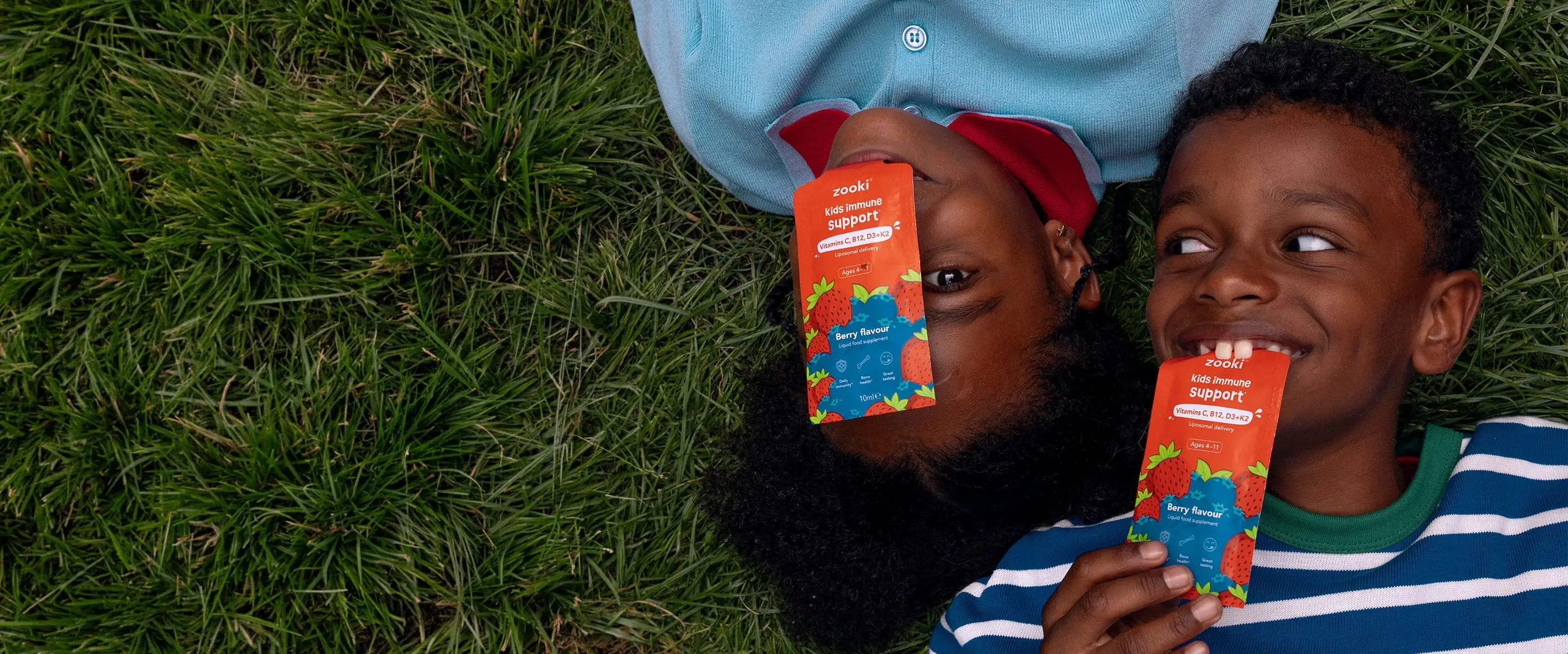 Two children lying on grass holding Zooki sachets