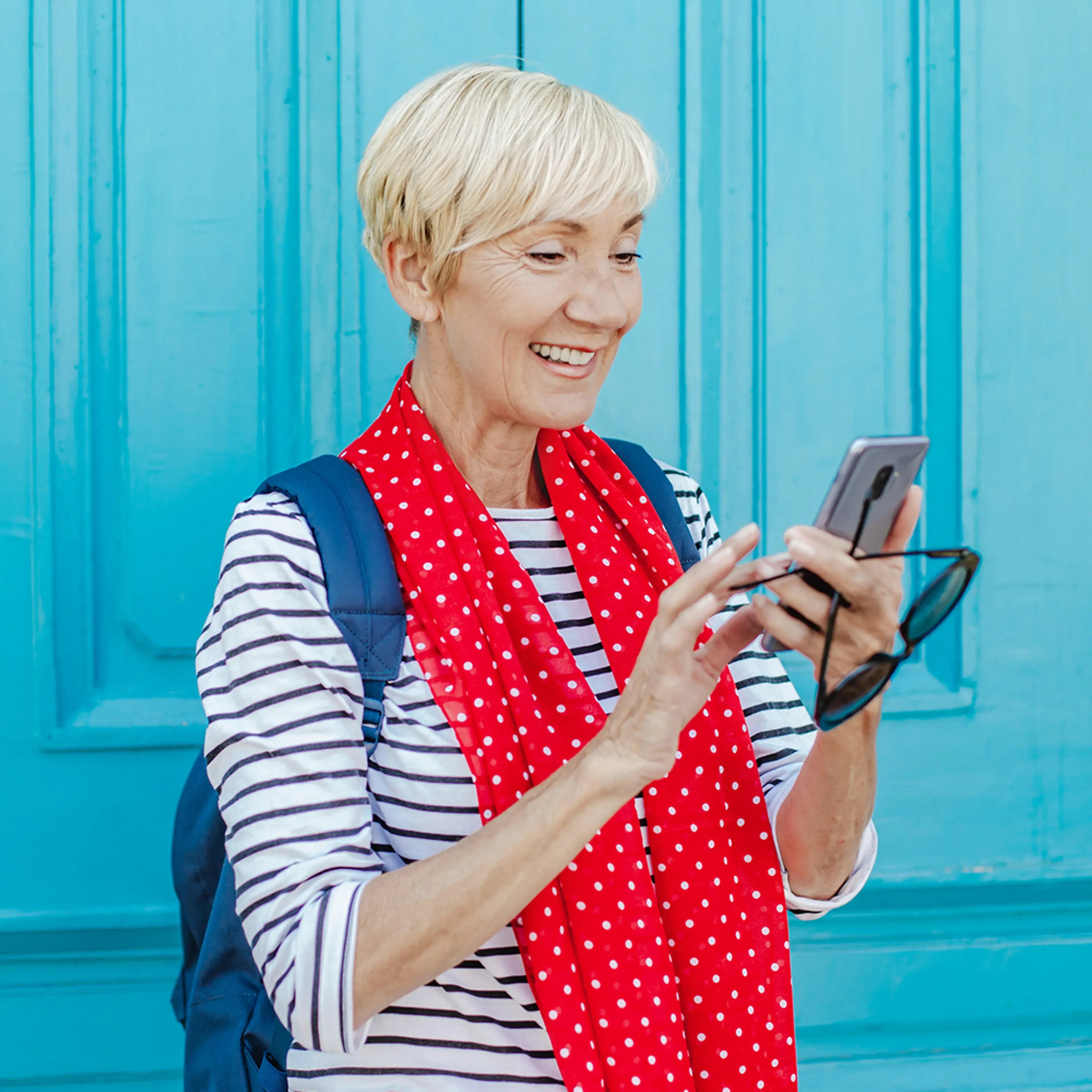 A woman with a backpack checking her phone against a blue painted wall