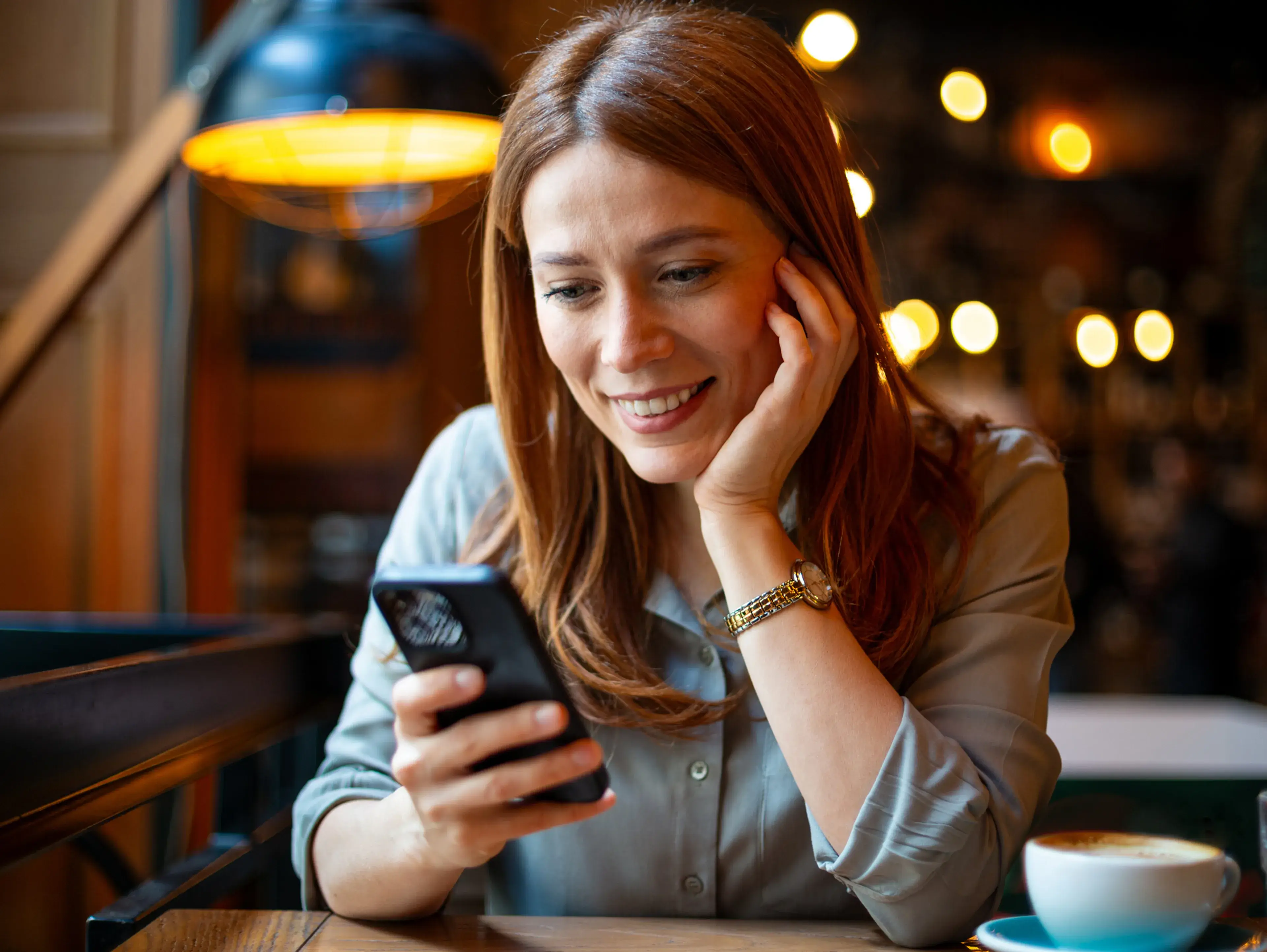 A woman in a café smiling at her phone