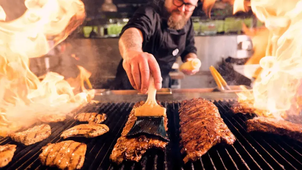 A chef basting ribs and chicken over a flaming grill