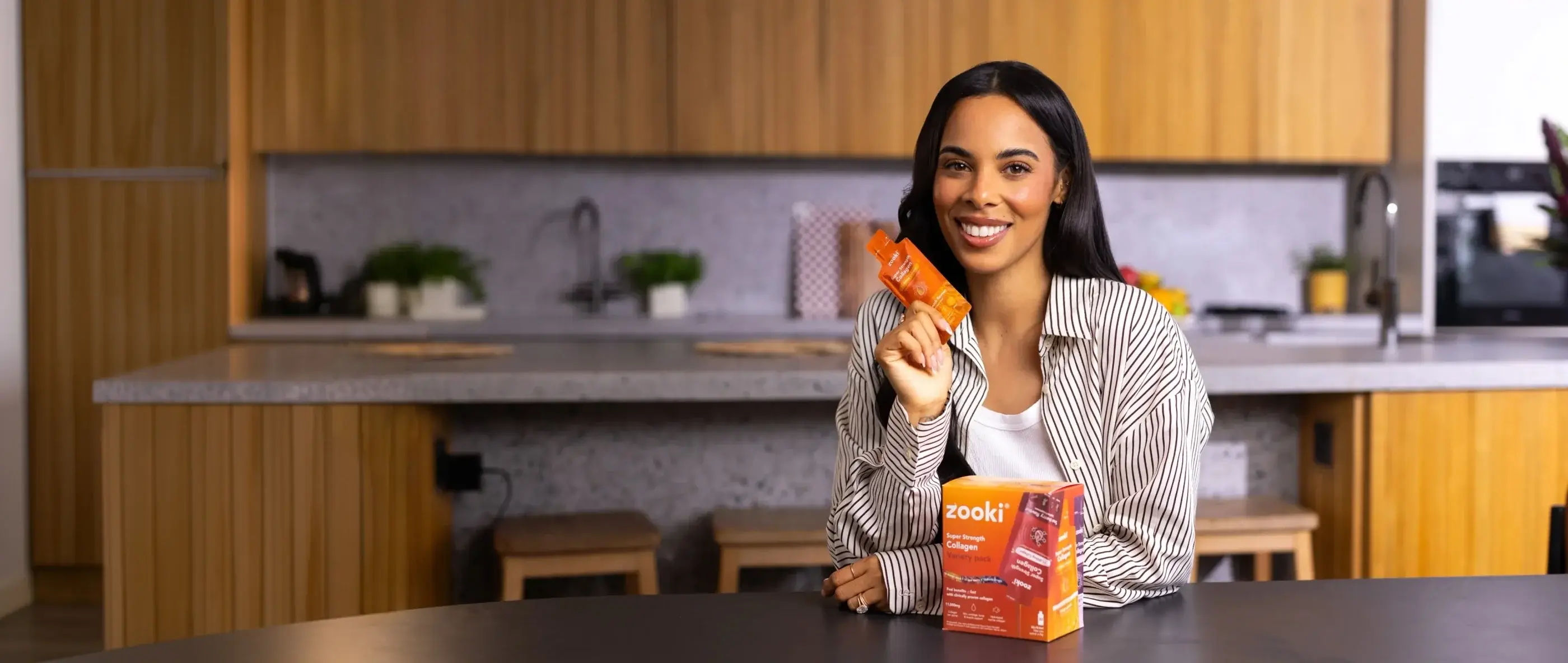 A woman in a kitchen holding a Zooki sachet, product boxes on the counter