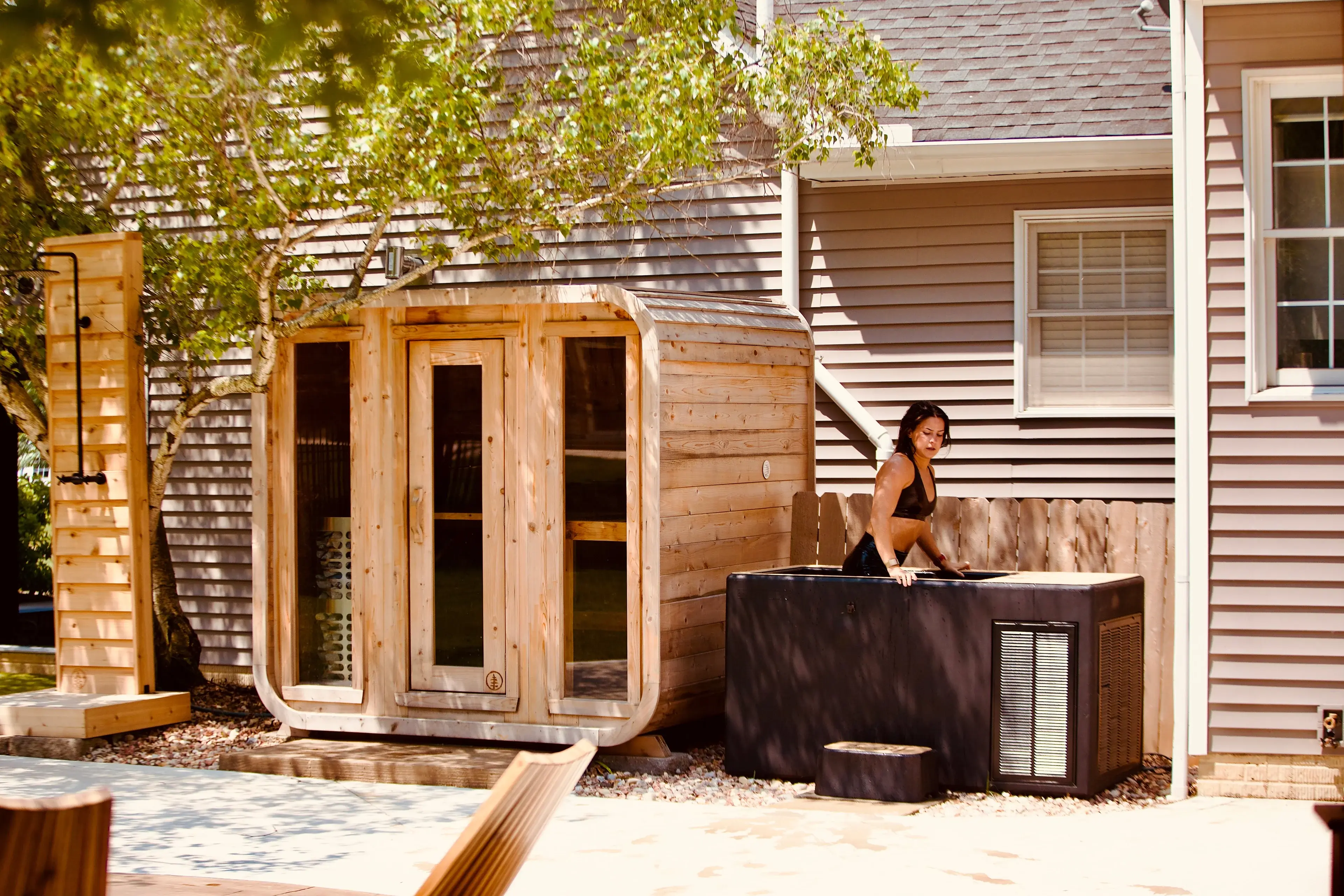 A cedar barrel sauna and a cold plunge tub set up beside a house