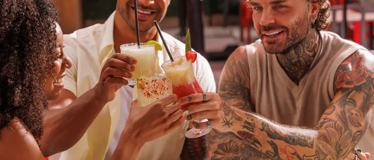 Three people clinking cocktails across a table