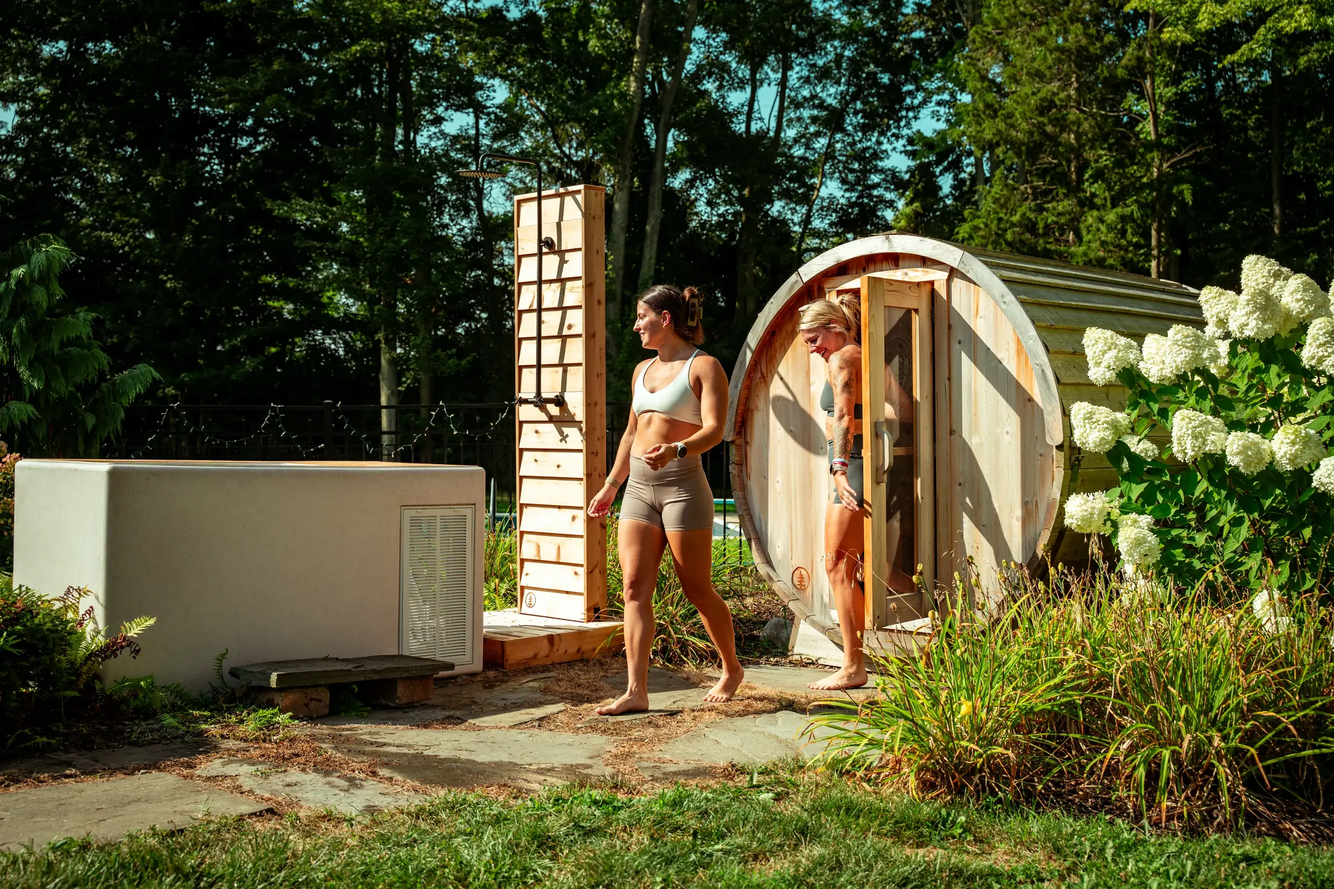 A woman standing beside an outdoor sauna cabin in a garden