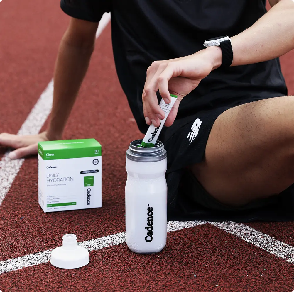 A runner kneeling on a track beside a Daily Hydration box and a bottle
